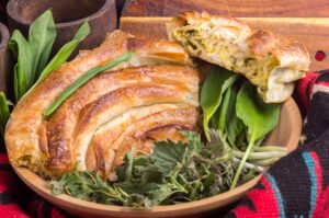 Delicious homemade pie with wild garlic, freshly baked to golden perfection, served on a rustic wooden table in Katun Reljina