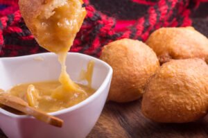 Close-up of golden fried dough (Priganice) dipped in honey, served on a wooden table with a rustic red and black textile backdrop